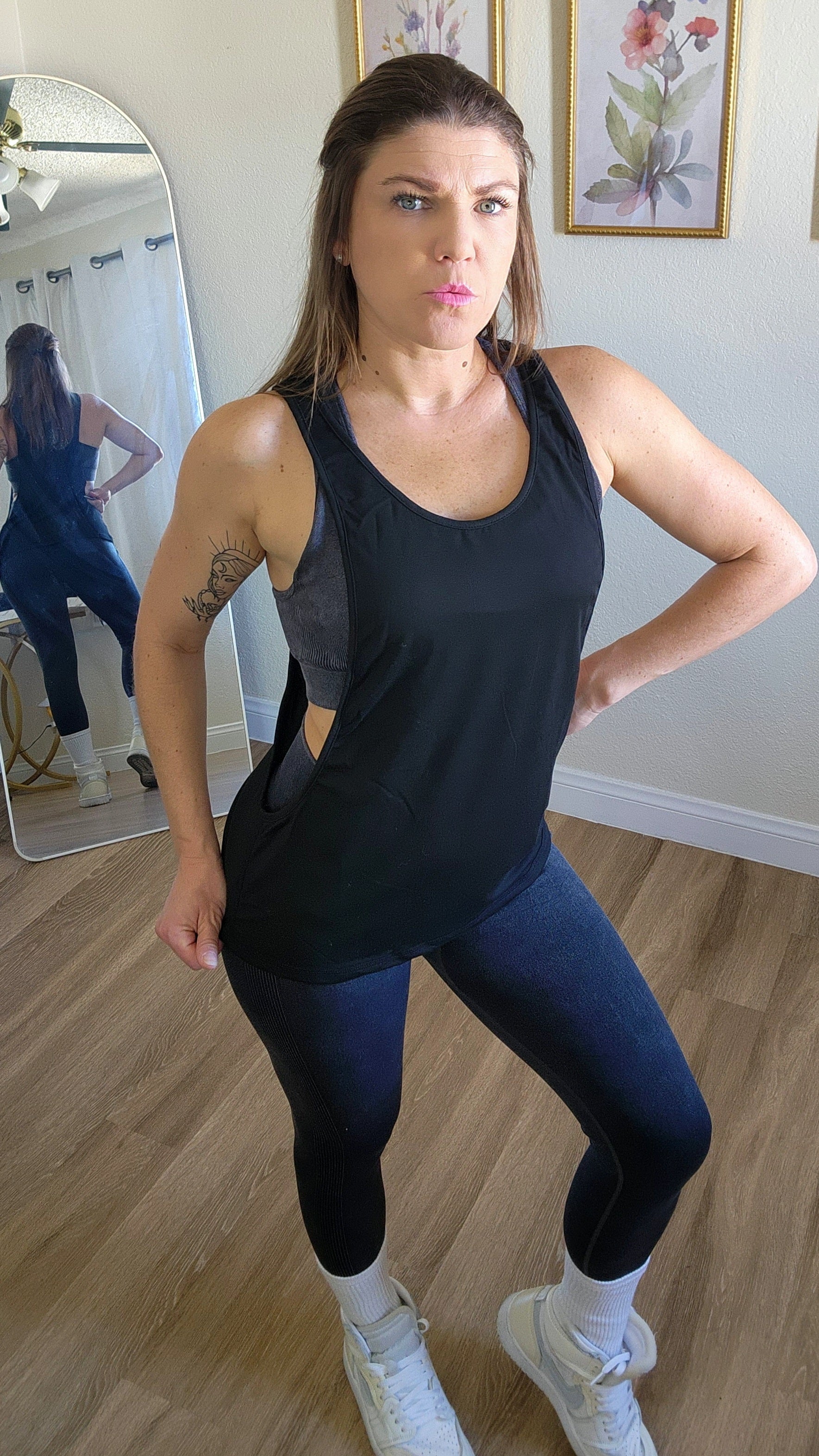 Woman in black tank top and leggings posing in a room with a mirror.