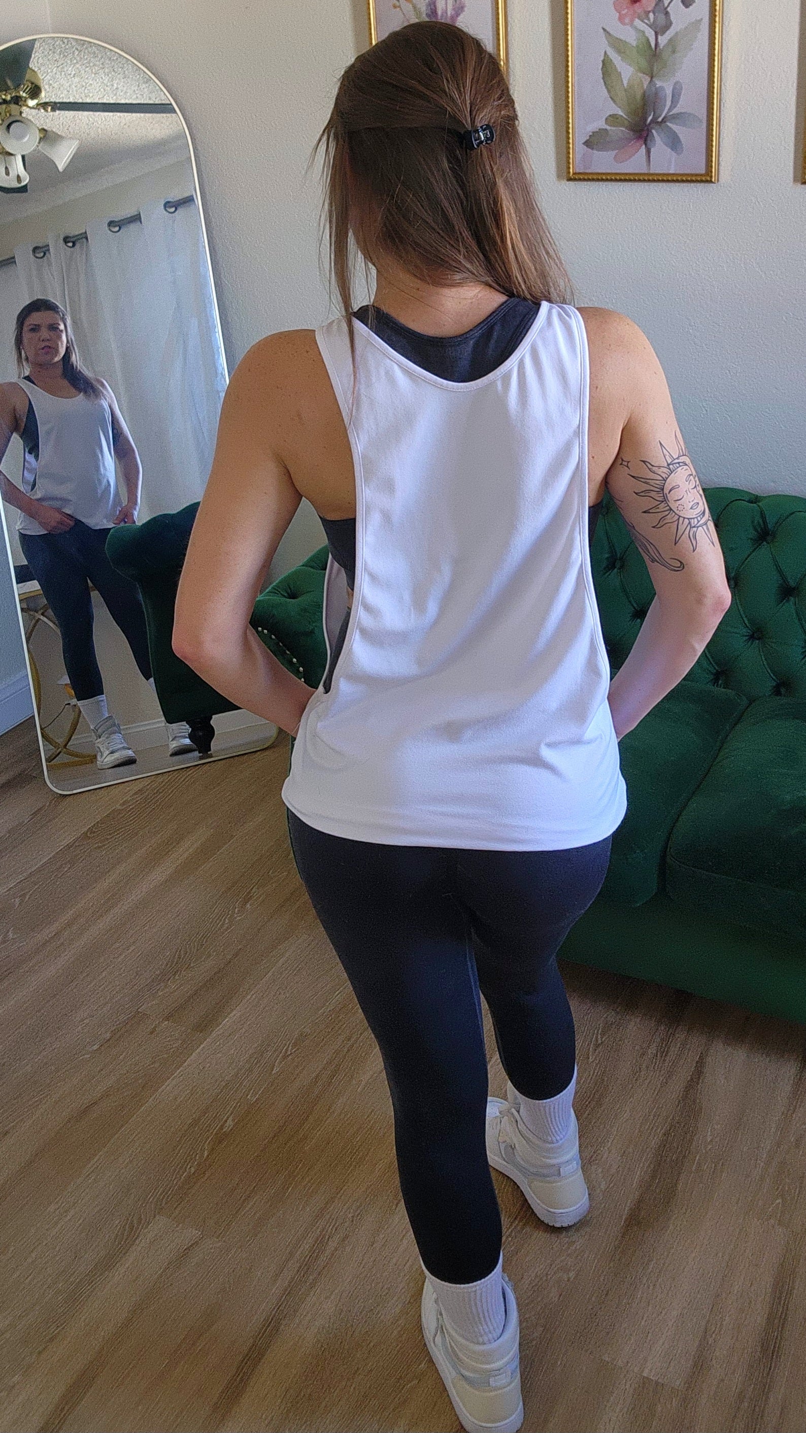 Woman in black tank top and leggings posing in a room with a mirror.
