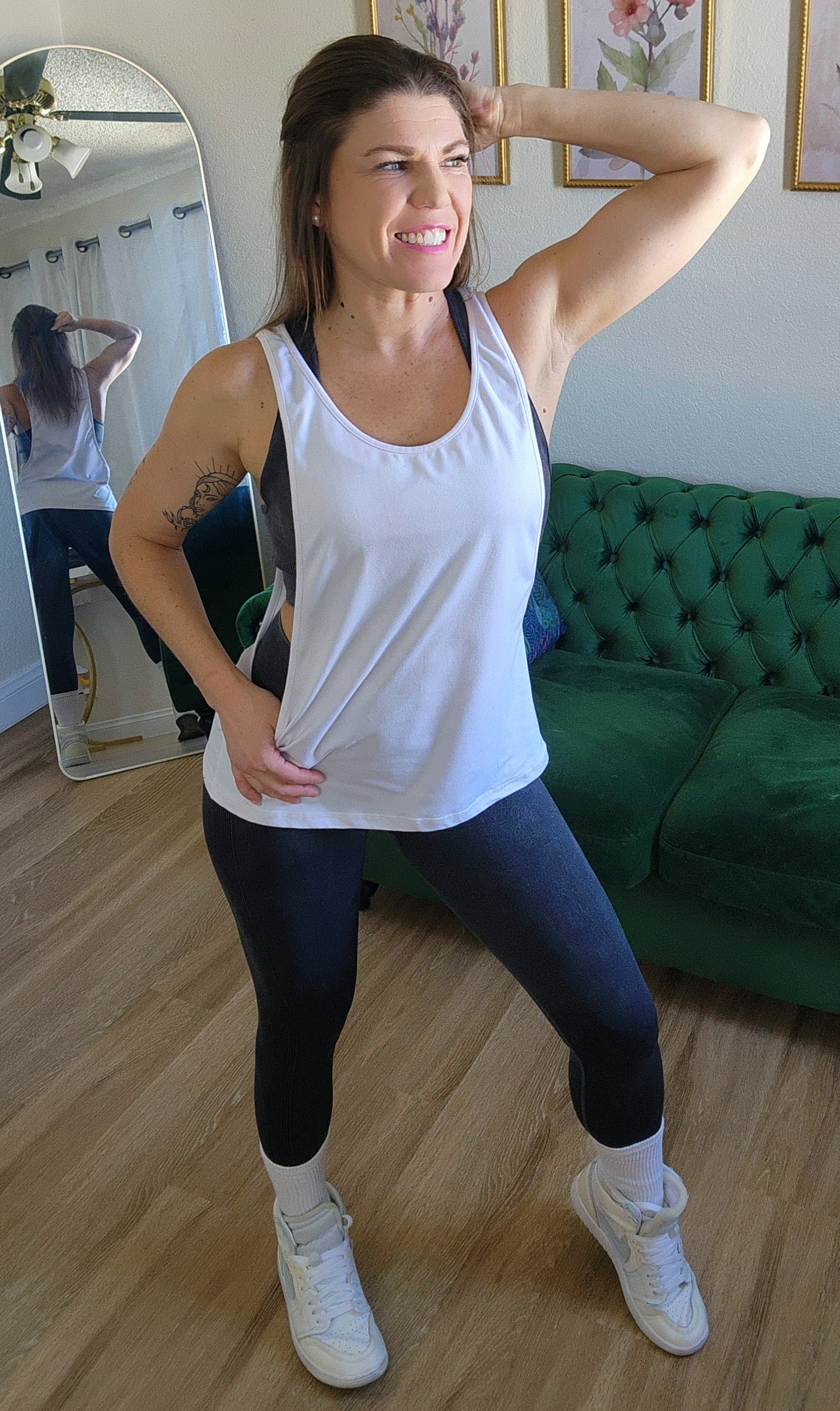 Woman in black tank top and leggings posing in a room with a mirror.